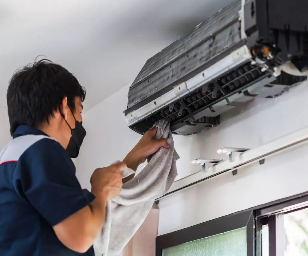 A picture of a man cleaning the coils in a mini split AC with homemade AC coil cleaner