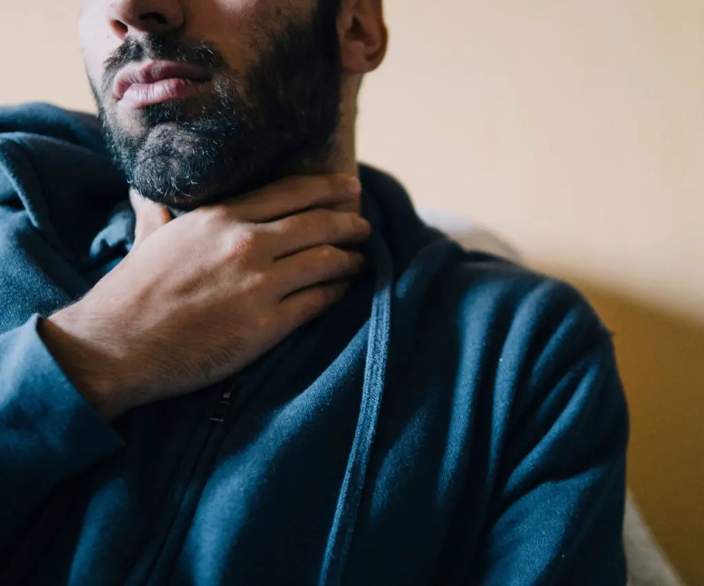 man rubbing his neck because of a sore throat caused by the AC